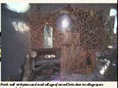 North wall with piano and wood collage of carved 2x4s; door in collage opens into secret back room.